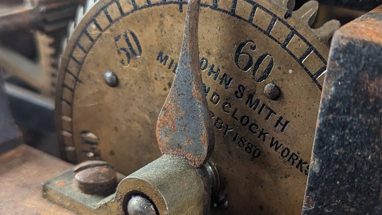 Part of the inside of a clock: brass cogs marked with seconds and a pointer